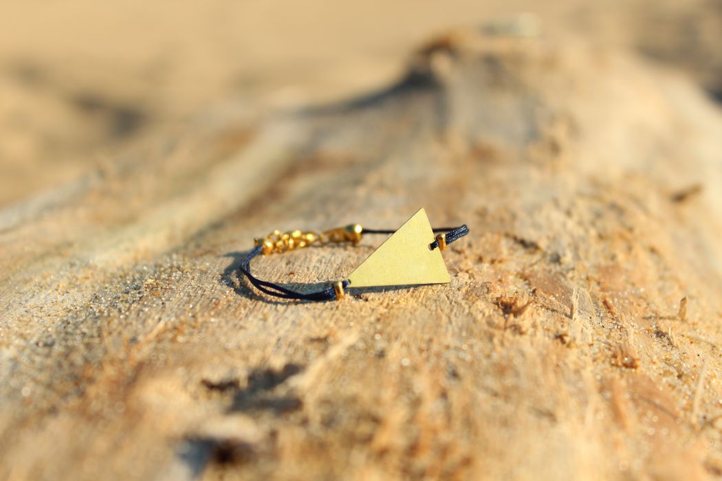 Le bracelet KANTI Marine, triangle doré et fil de jade, sur le bois flotté de la plage d'Hossegor. Existe dans d'autres coloris.