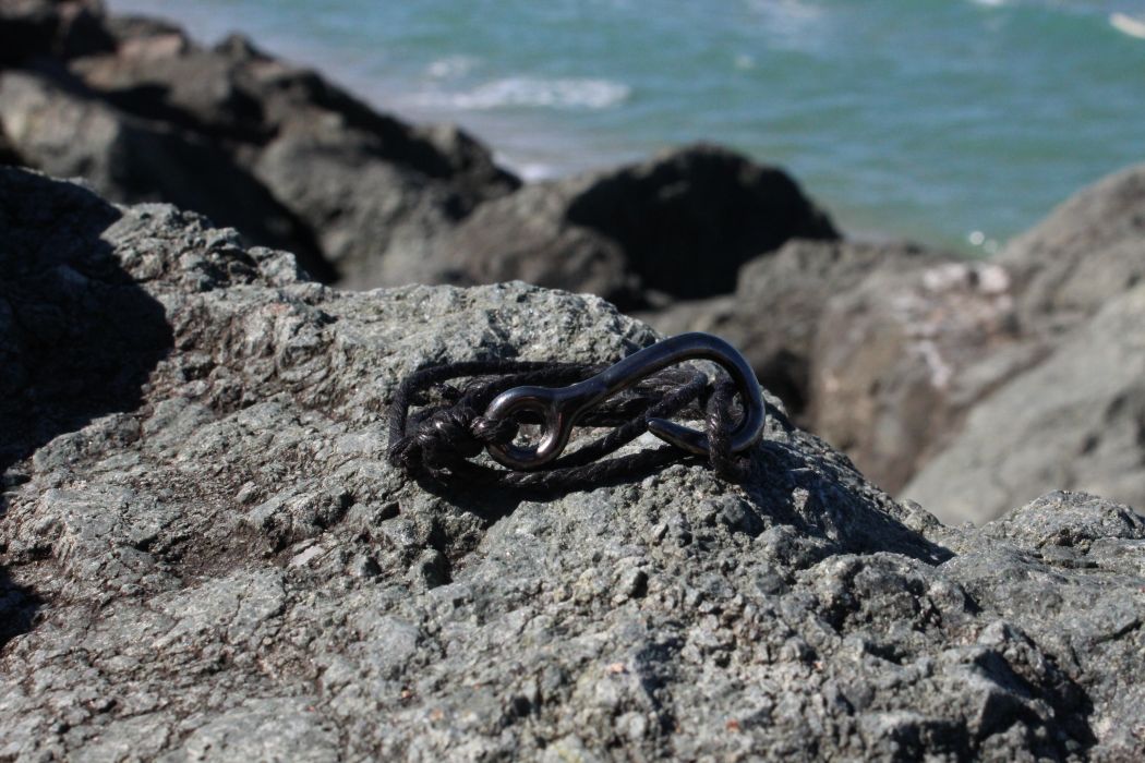 Bracelet KATSI tout noir, hameçon et cordage, sur les rochers de Biarritz. Existe dans d'autres coloris.